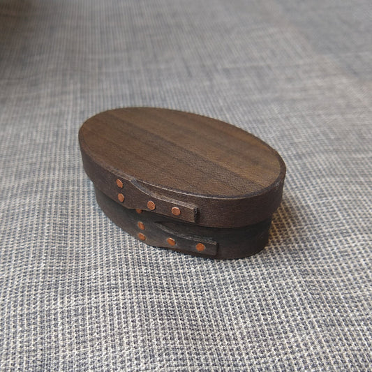 Handmade wooden Shaker oval #00 box with a black/grey outside and a natural maple inside, on a gray tablecloth