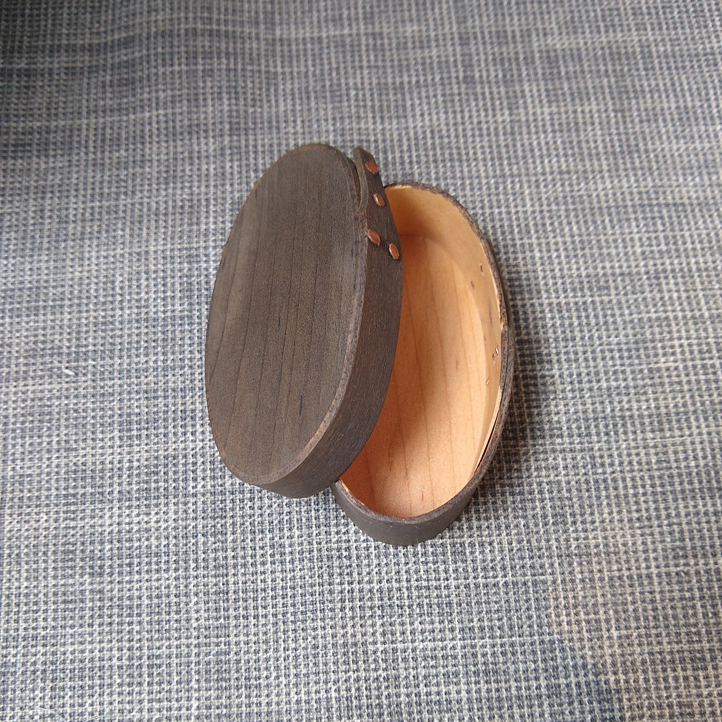 Handmade wooden Shaker oval #00 box with a black/grey outside and a natural maple inside, on a gray tablecloth