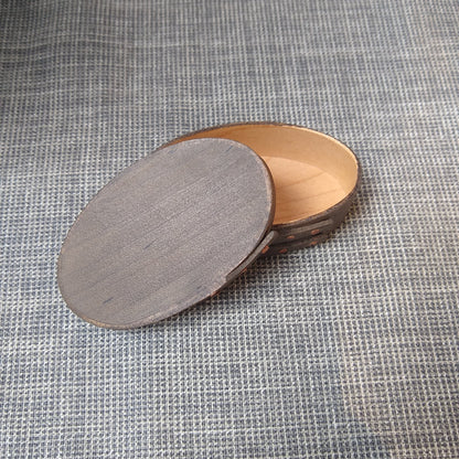 Handmade wooden Shaker oval #00 box with a black/grey outside and a natural maple inside, on a gray tablecloth