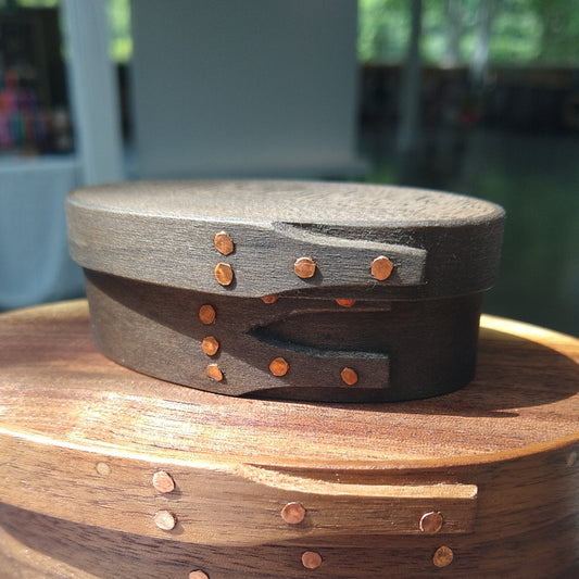 Handmade wooden Shaker oval #00 box with a black/grey outside and a natural maple inside, on a gray tablecloth