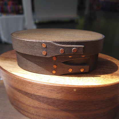 Handmade wooden Shaker oval #00 box with a black/grey outside and a natural maple inside, on a gray tablecloth