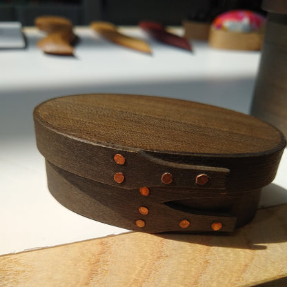Handmade wooden Shaker oval #00 box with a black/grey outside and a natural maple inside, on a gray tablecloth